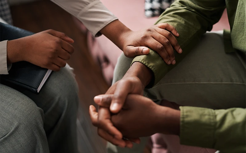 Two people sitting side by side, one offering a comforting touch on the other's arm.