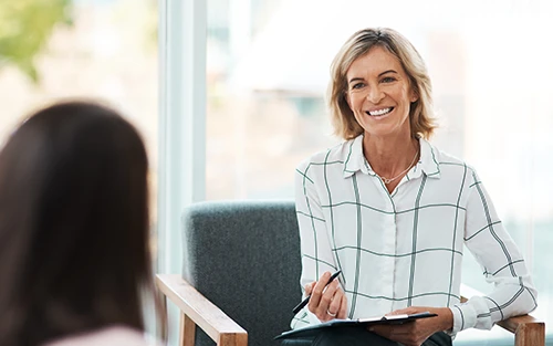 Smiling therapist with a notebook in a bright, indoor setting.