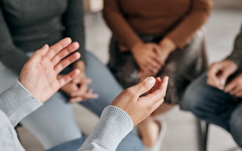 People sitting in a circle, with focus on gesturing hands in the foreground.